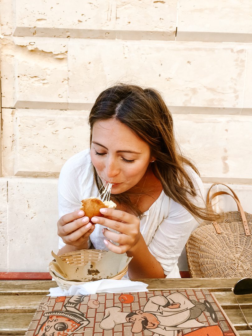A girl enjoying a cheesy bite of an arancini di riso, a food you need to try while travelling through this 7-day Sicily itinerary