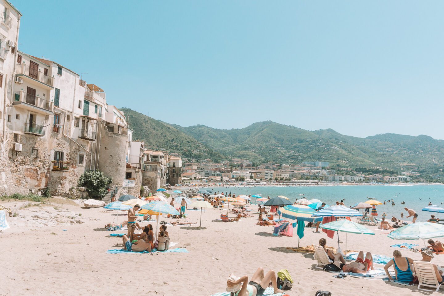 People and colourful umbrellas scattered along the Cefalu beach in -- an amazing stop on this 7-day Sicily Itinerary