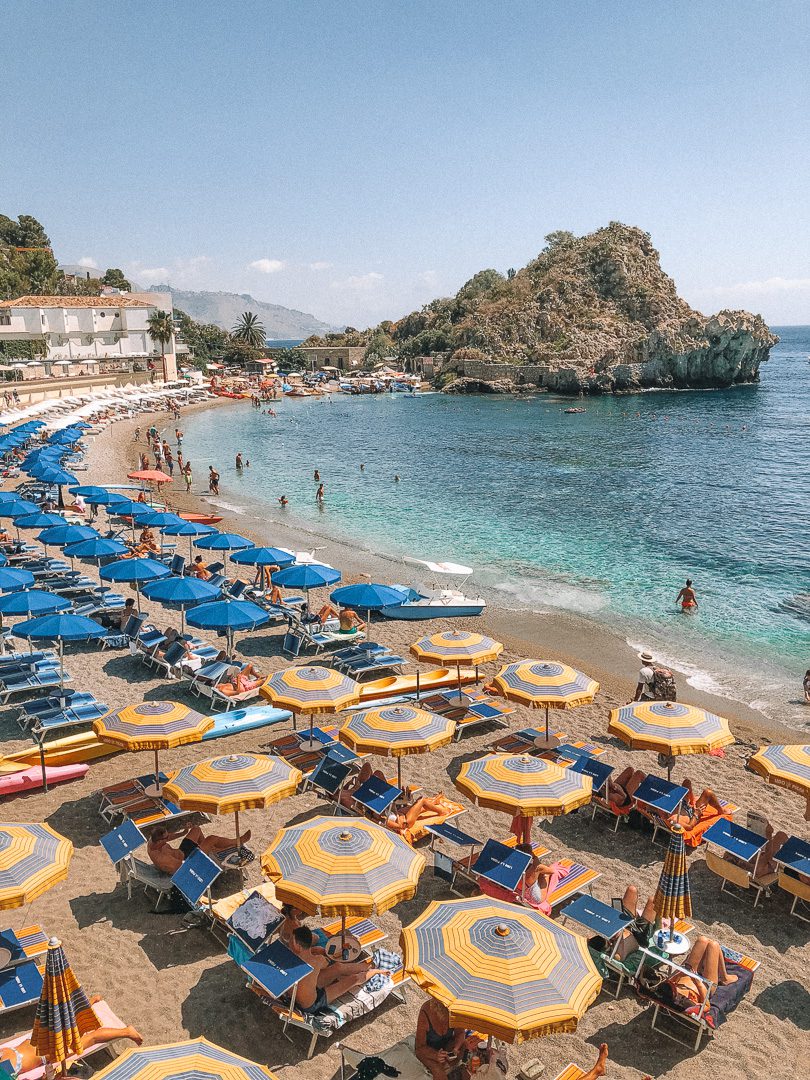 Blue and yellow umbrellas and sun chairs at the beautiful Mazzaro Bay beach in Taormina, Sicily, southern Italy.