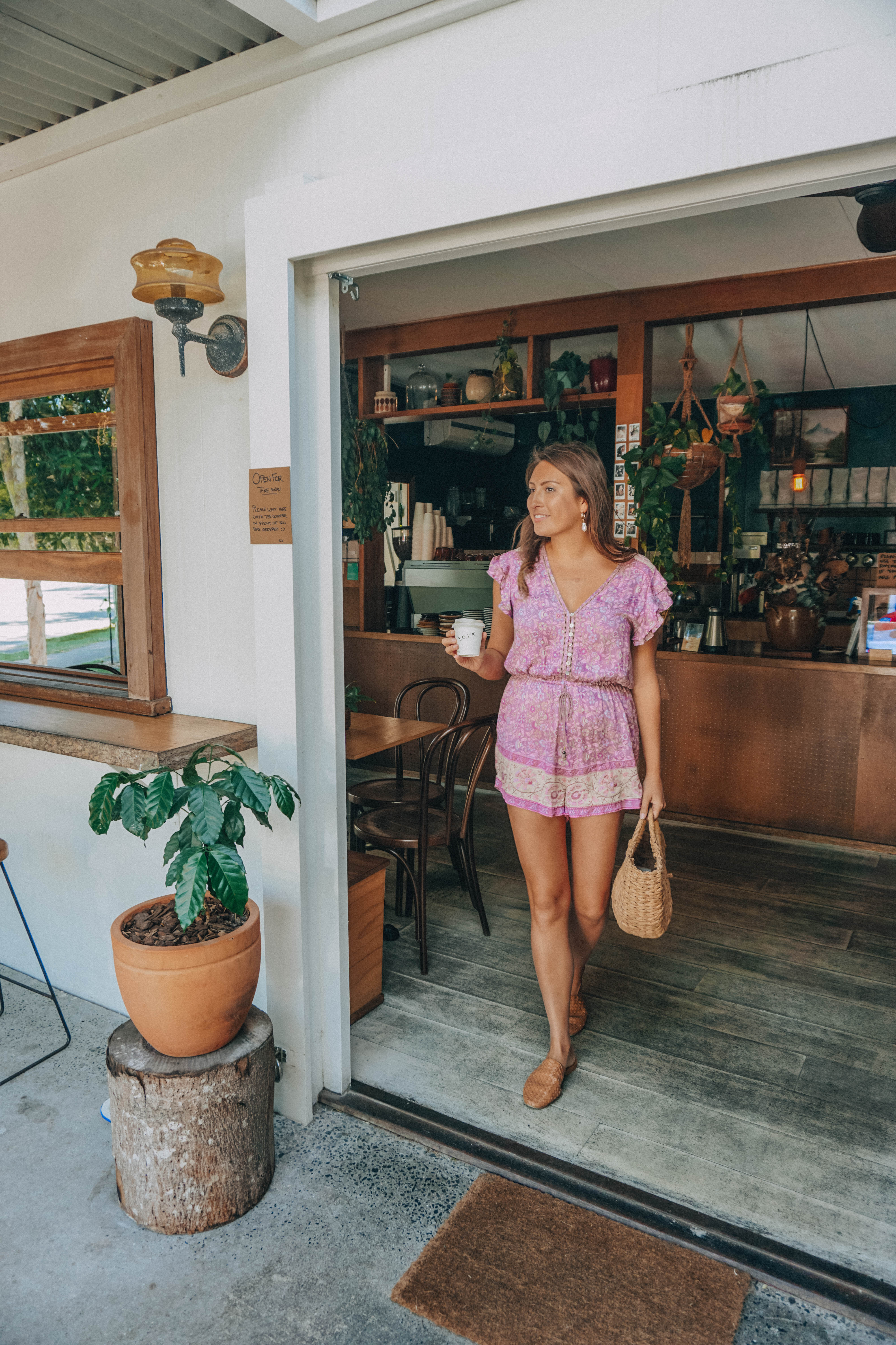 A girl walking out of Folk in Byron Bay with a coffee