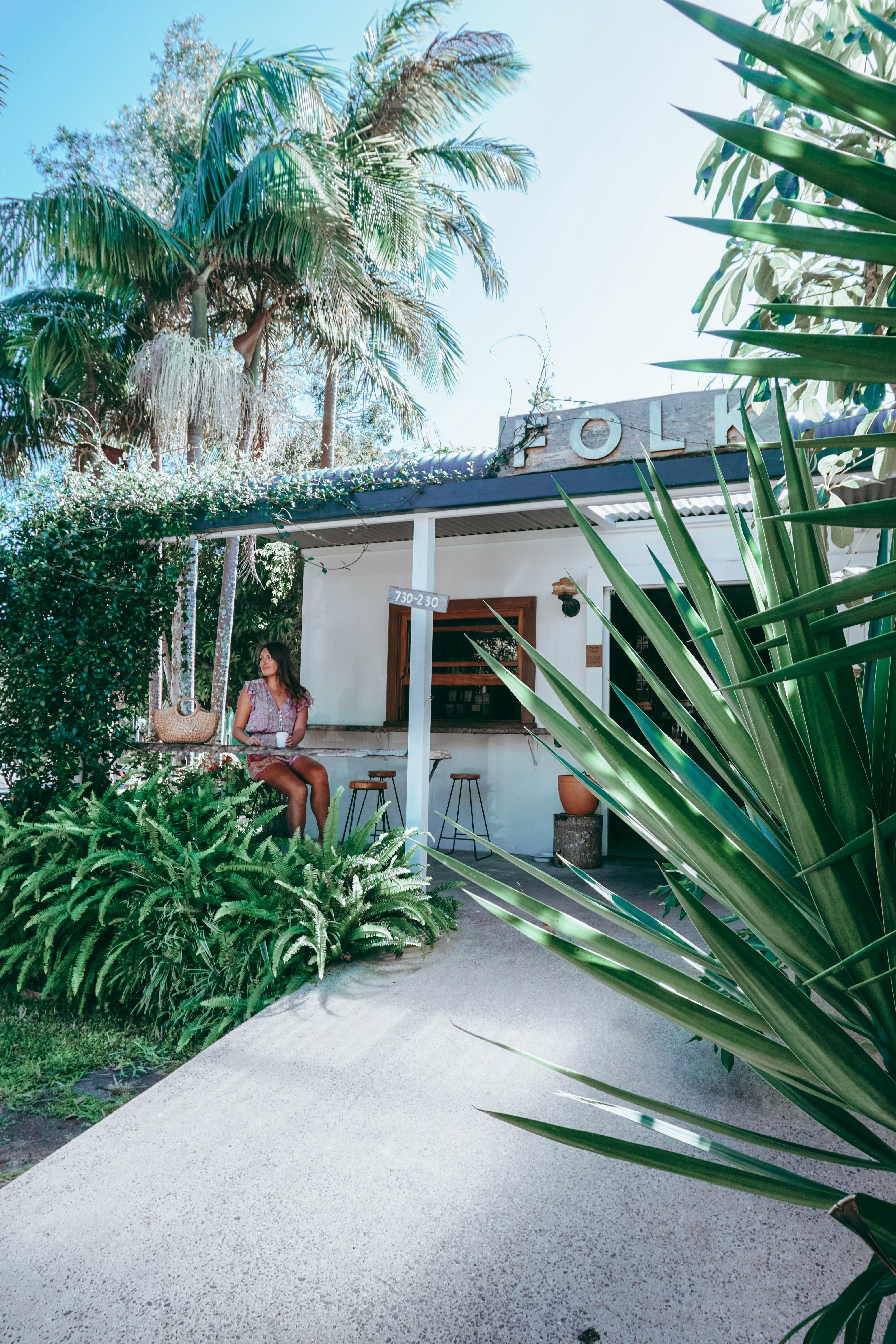 A girl sitting at a bench seat drinking a coffee at Folk cafe in Byron Bay 