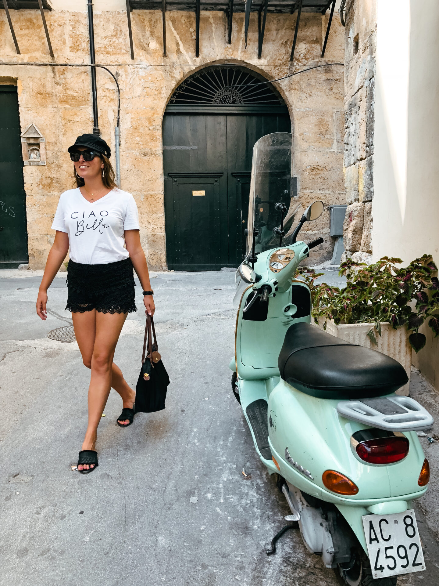 A girl walks past a mint green vespa in Palermo.