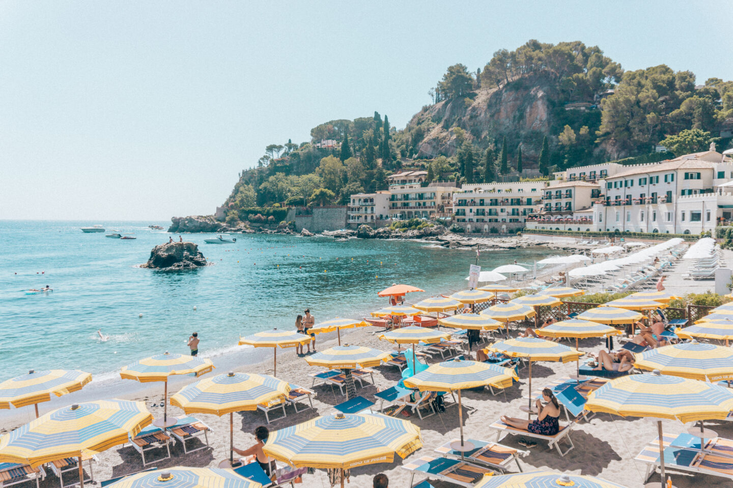 Blue and yellow umbrellas and sun chairs at the beautiful Mazzaro Bay beach in Taormina - a must stop on this 7-day Sicily Itinerary.