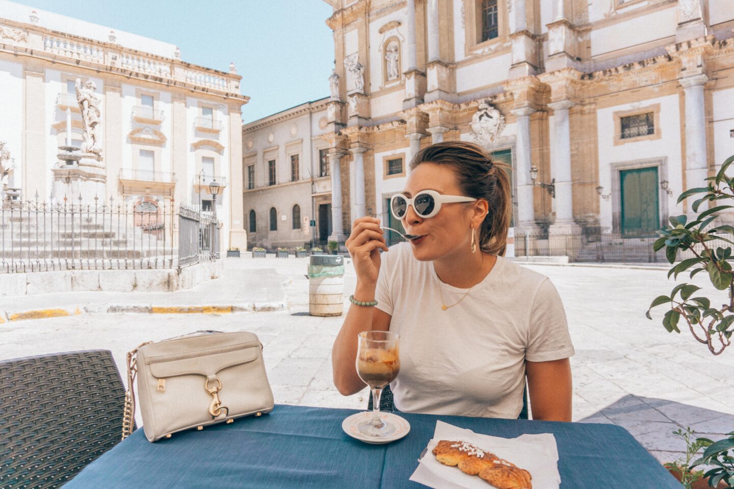A girl wearing white sunglasses and t-shirt eats an Italian affogato coffee in a square in Palermo, Sicily