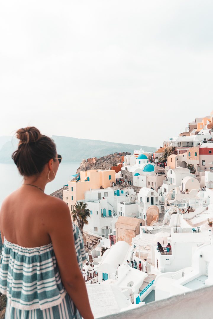 A girl stands and admires the iconic blue and white washed towns on Santorini island in Greece.