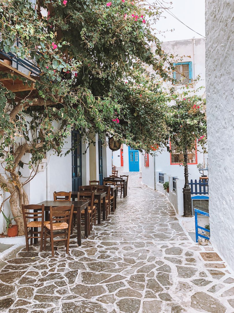 During 10 Days in Greece Itinerary a girl shops in Santorini where the store front is white with blue doors, and flowering bougainvillea.