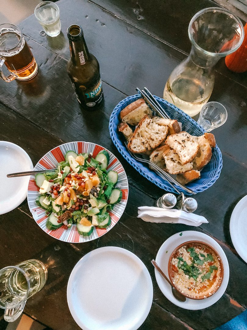 Looking down at a table of traditional Greek food including dakos and hummus, and wine. 