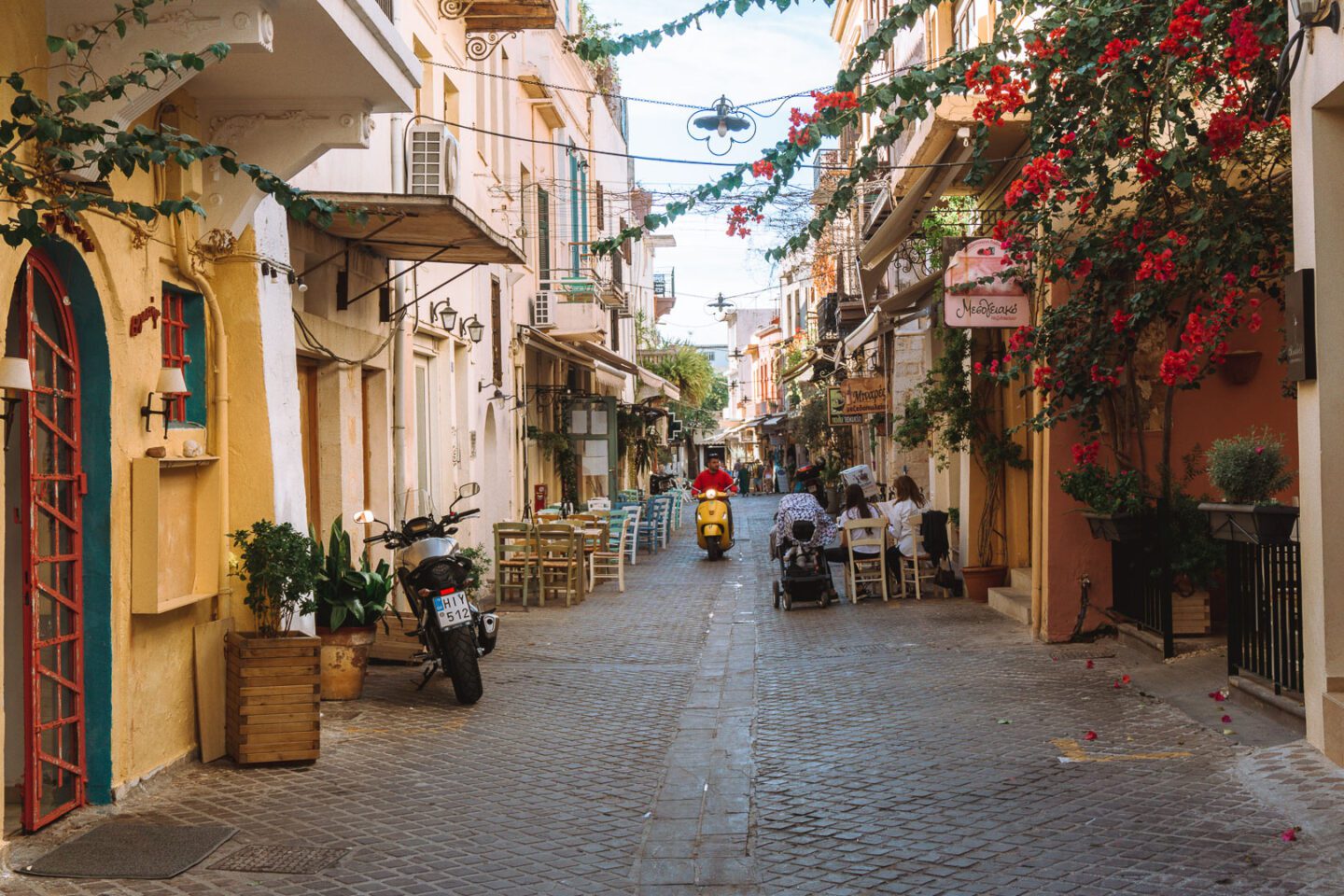 A man on a yellow vespa rides through the quiet old town of Chania Crete. 