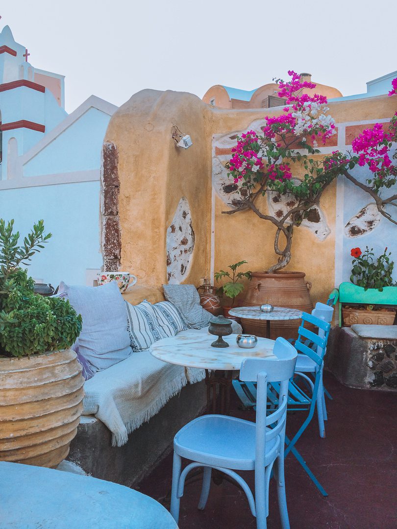 10 Days in Greece Itinerary - A beautiful restaurant patio in Greece with colourful tables, chairs, cushions.
