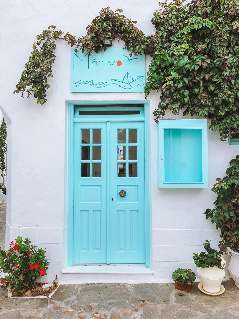 A bright blue boutique door with vines growing over the white walls - an iconic look when travelling Greece