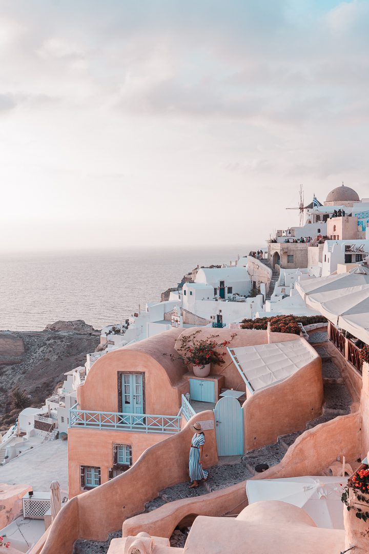 A girl walks past a pink villa in Oia during a sunset on Santorini Island in Greece.