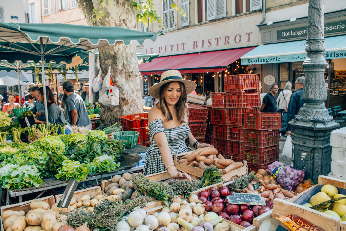 A girl in a hat and gingham dress picks vegetables from the local Farmers Market in Aix-en-Provence in France.