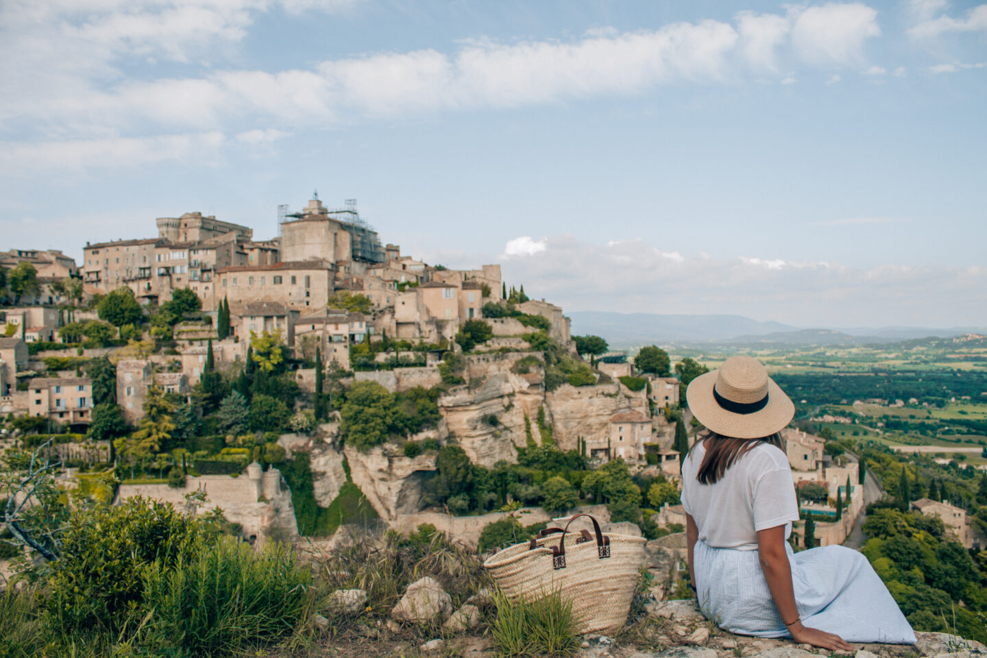 A girl with a hat on sits on a vista looking at the one of the top places in to visit France, the village of Gordes.