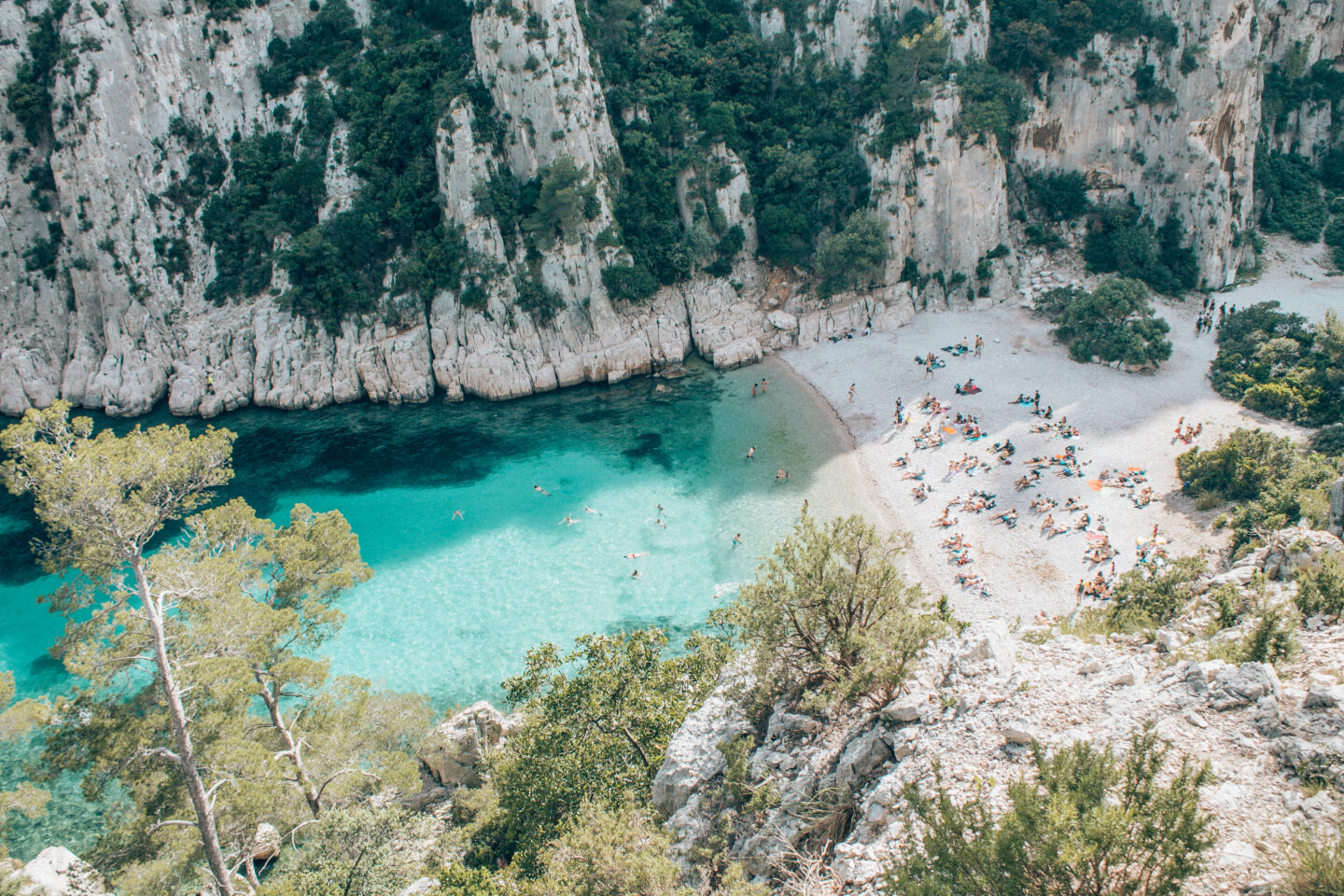Looking down at the rocky cliffs, turquoise waters and bathers on one of the secluded beaches of Calanques National Park in Cassis, France.