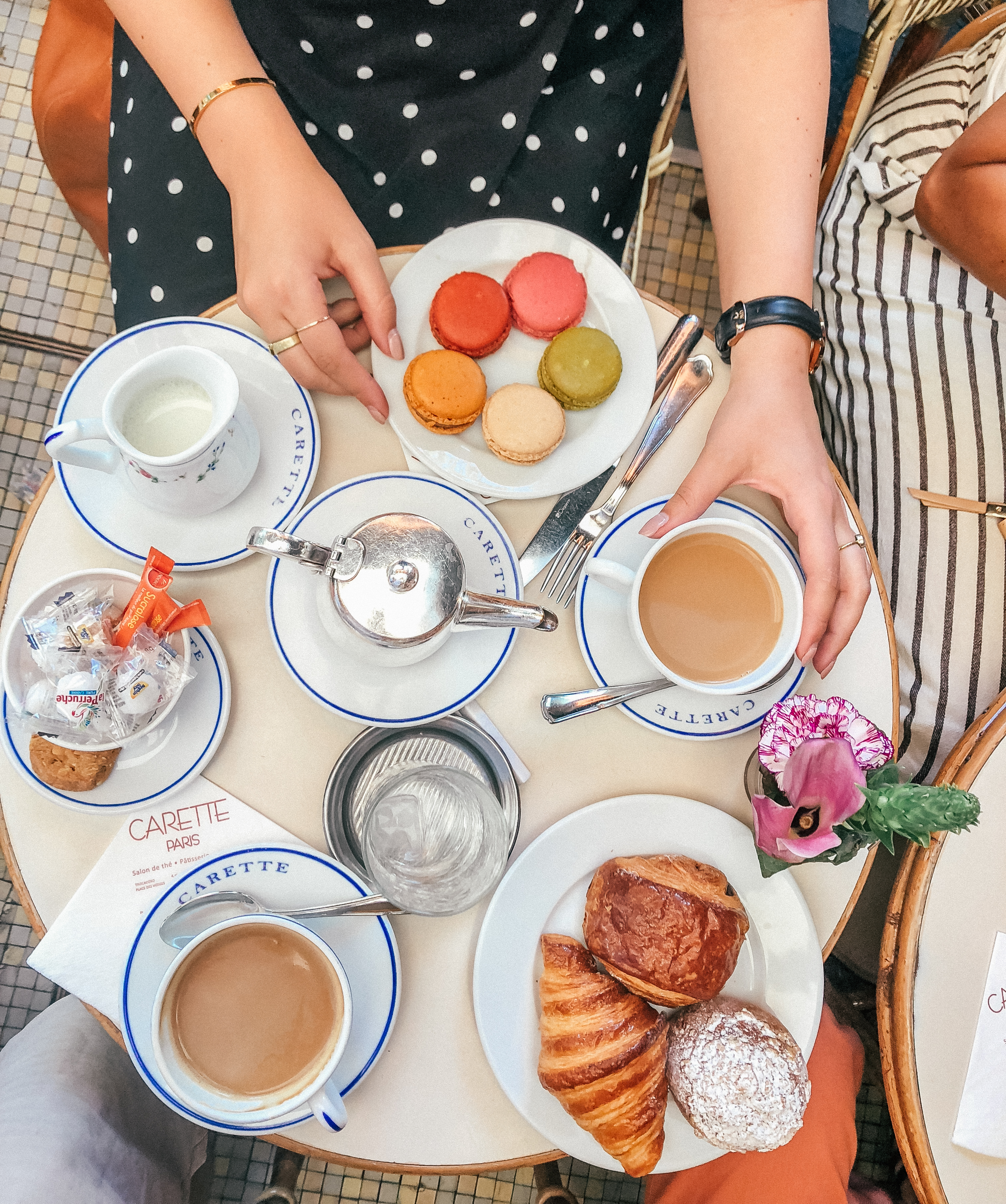 Looking down at a Parisian bistro table that has coffee, croissants, and macaroons. Cafes in Paris are definitely a place to visit while in France. 
