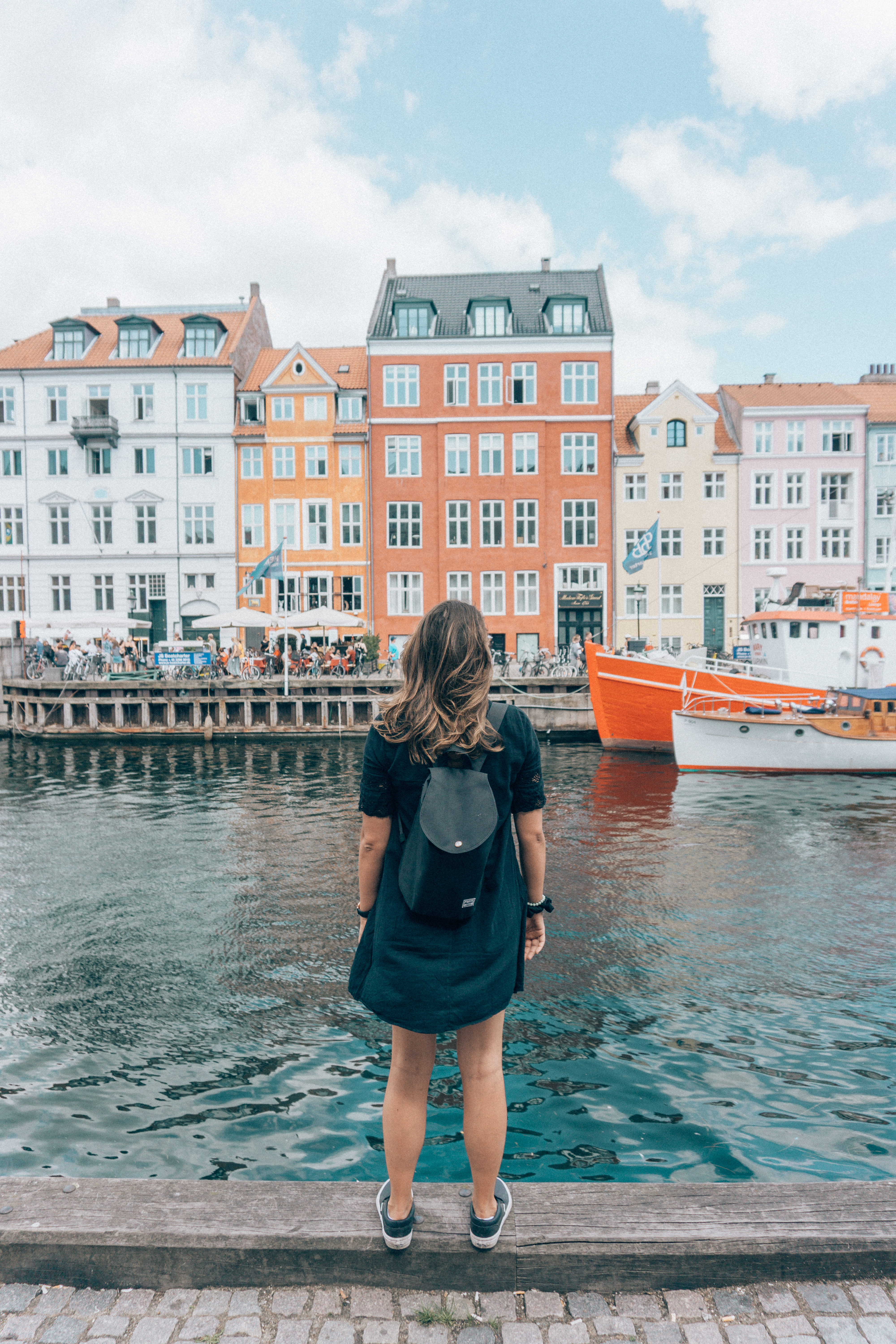 A girl takes a photo in front of the iconic and colourful Nyhavn buildings and boats in Copenhagen -a top thing to do for any tourist. 