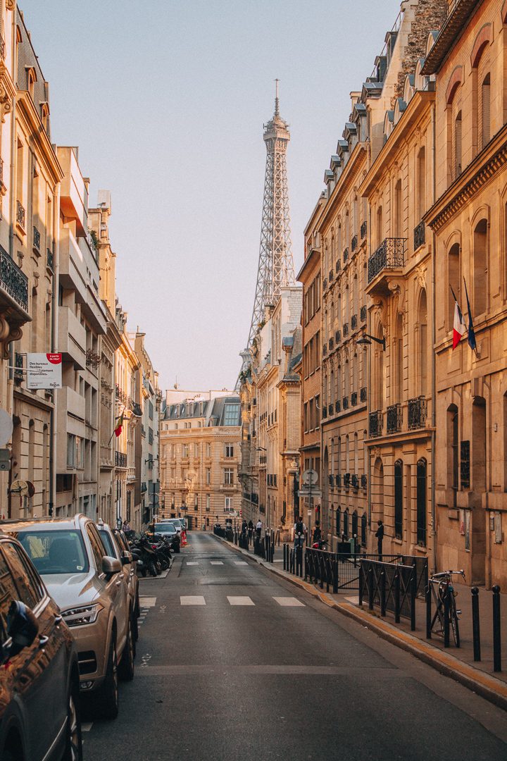 The iconic Eiffel Tower in the distance is framed amongst Parisian buildings at Golden Hour in Paris, France. 