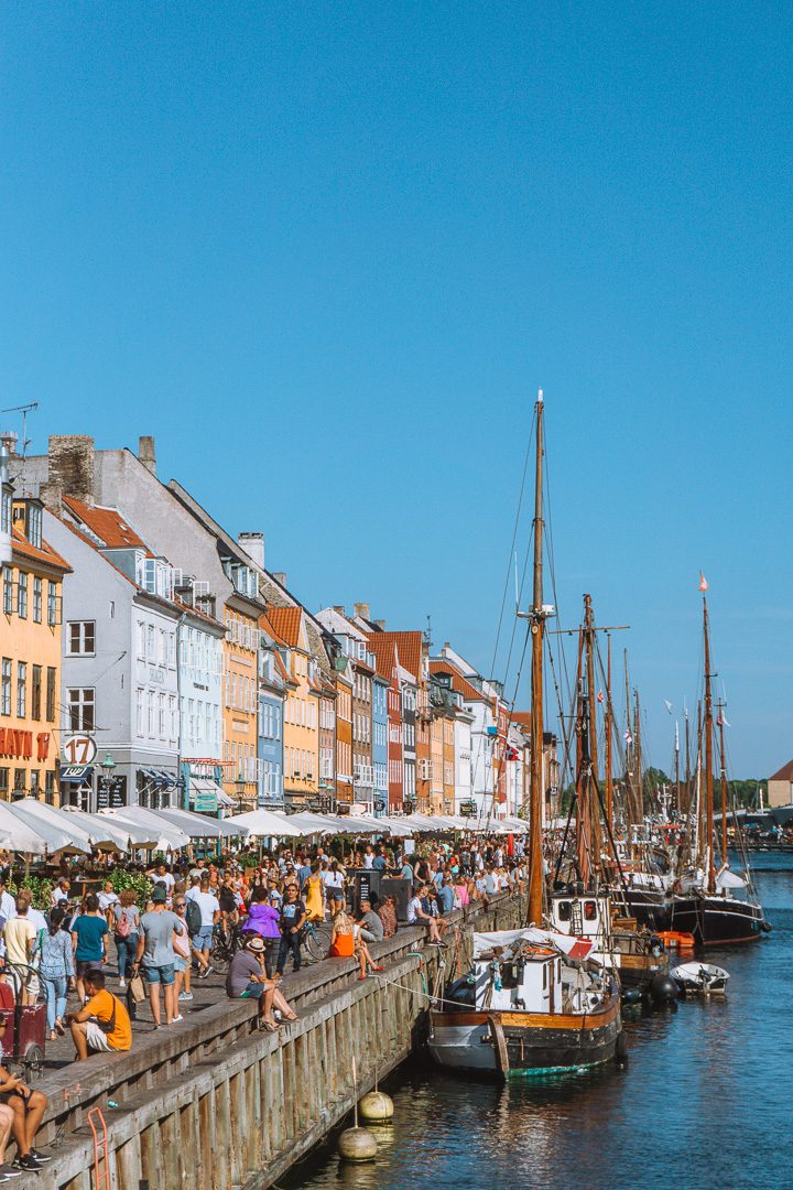 Tourist flood the streets of the iconic Copenhagen Nyhavn area, with old boats in the canals