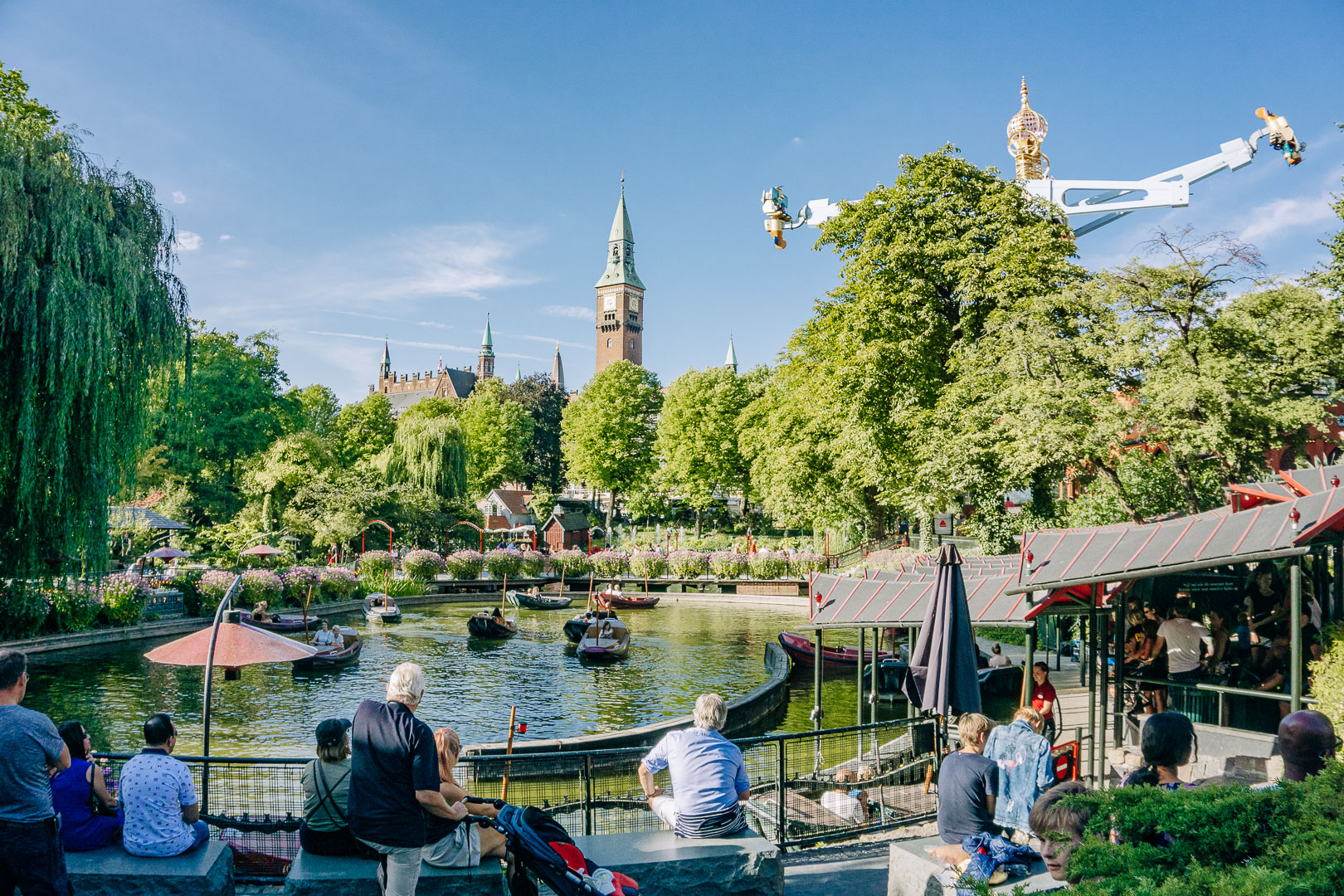 Tourists sit in Tivoli Gardens and admire the boats, and various rides from within the park. 