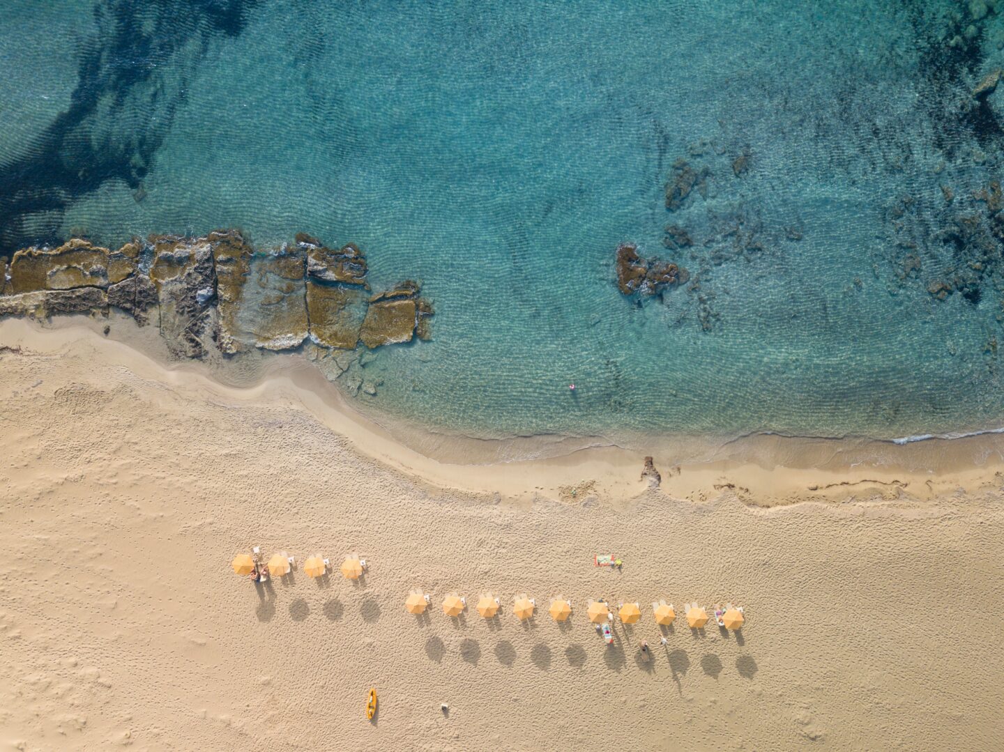 An aerial drone shot of a yellow umbrellas lined up on a beach in Crete, with its beautiful white sandy beaches, a clear turquoise waters. 