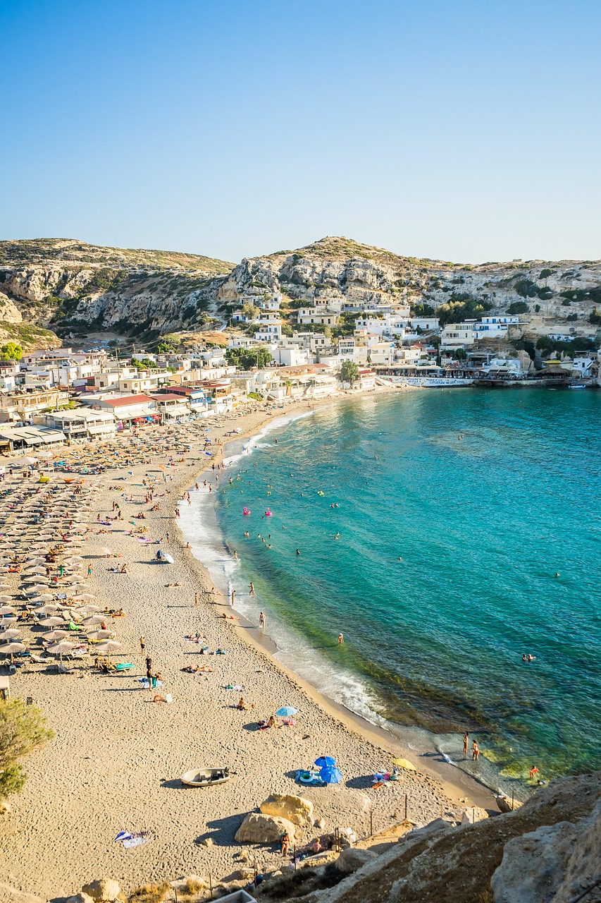 Beach goers enjoy the sunshine and blue waters of Matala, Greece on Crete Island.