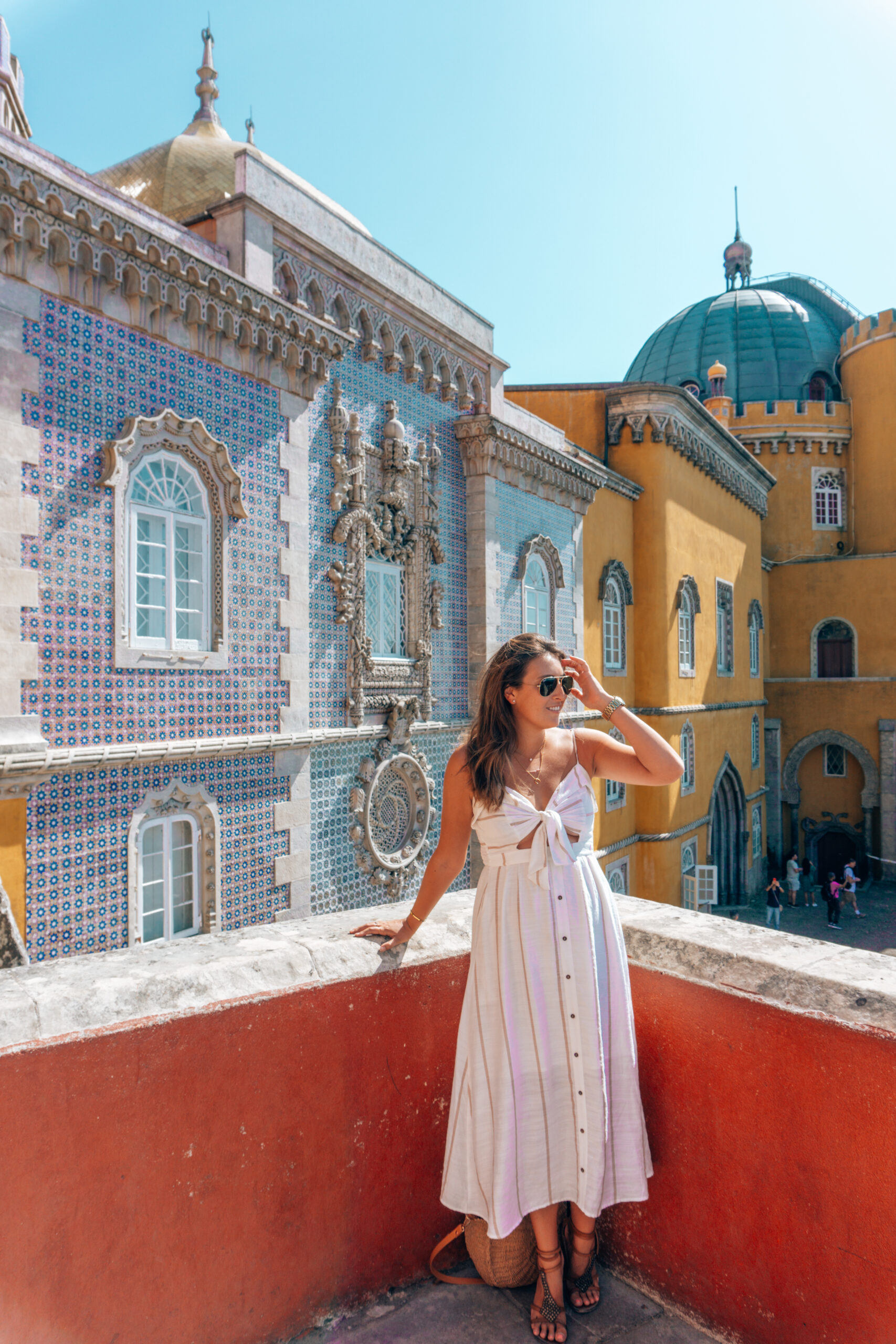 A girl in a white dress stands in front of the colourful Pena Palace in Sintra, a must see during your 3 days in Lisbon Itinerary 