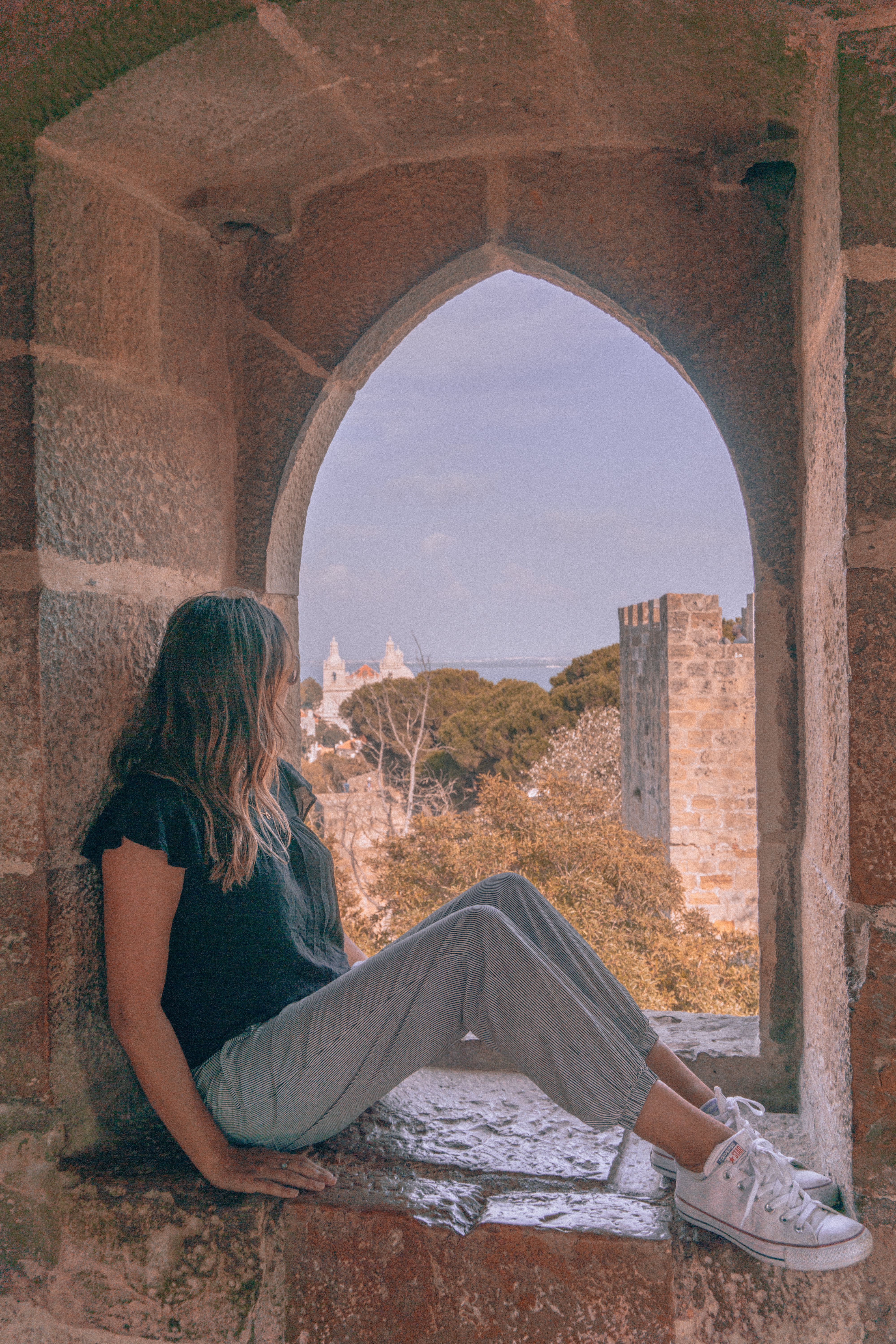 A girl sits in a window sill in São Jorge Castle and admires the views
