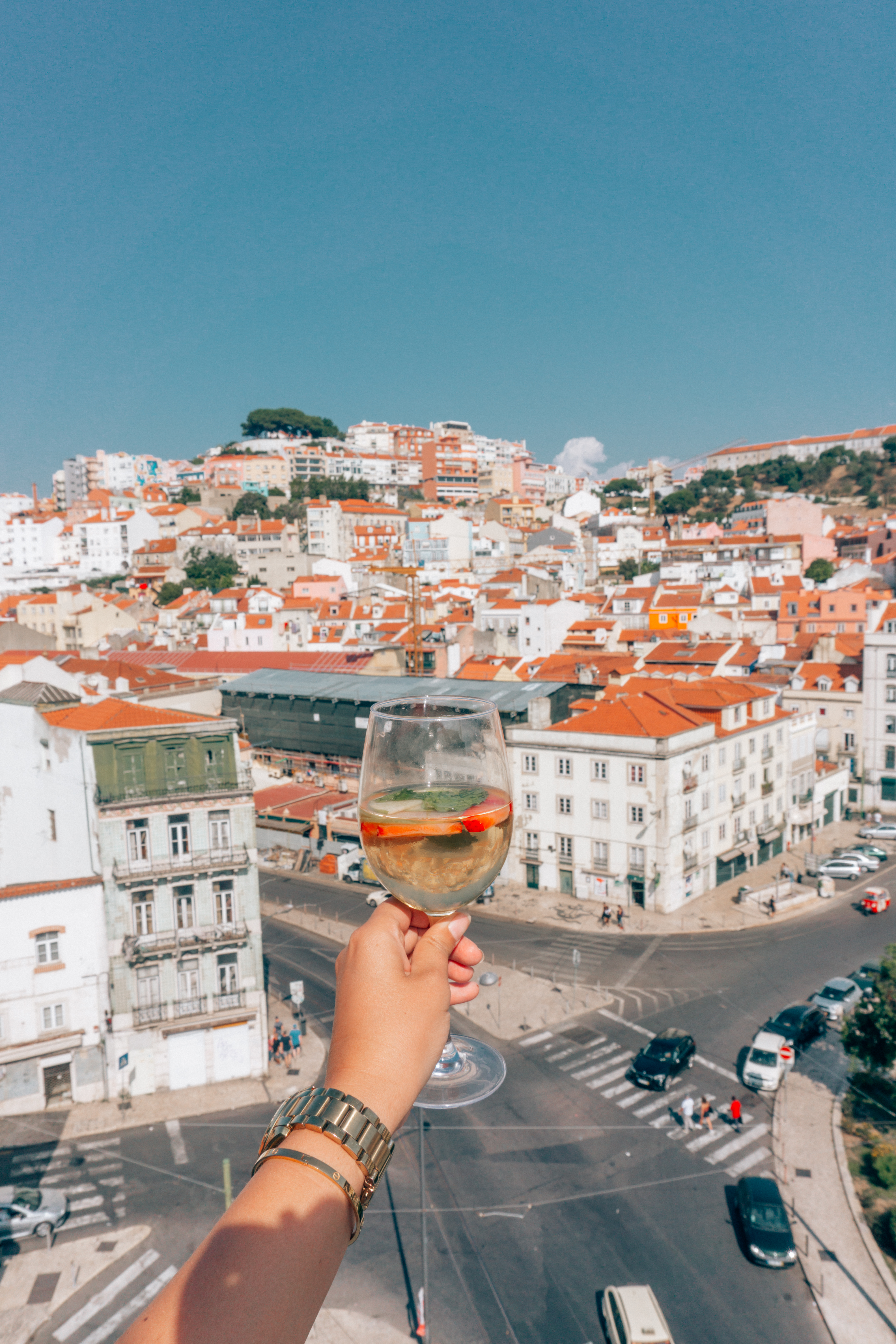 A girl holds a glass of white wine sangria from Topo rooftop bar looking out towards the red roofs of Lisbon Portugal
