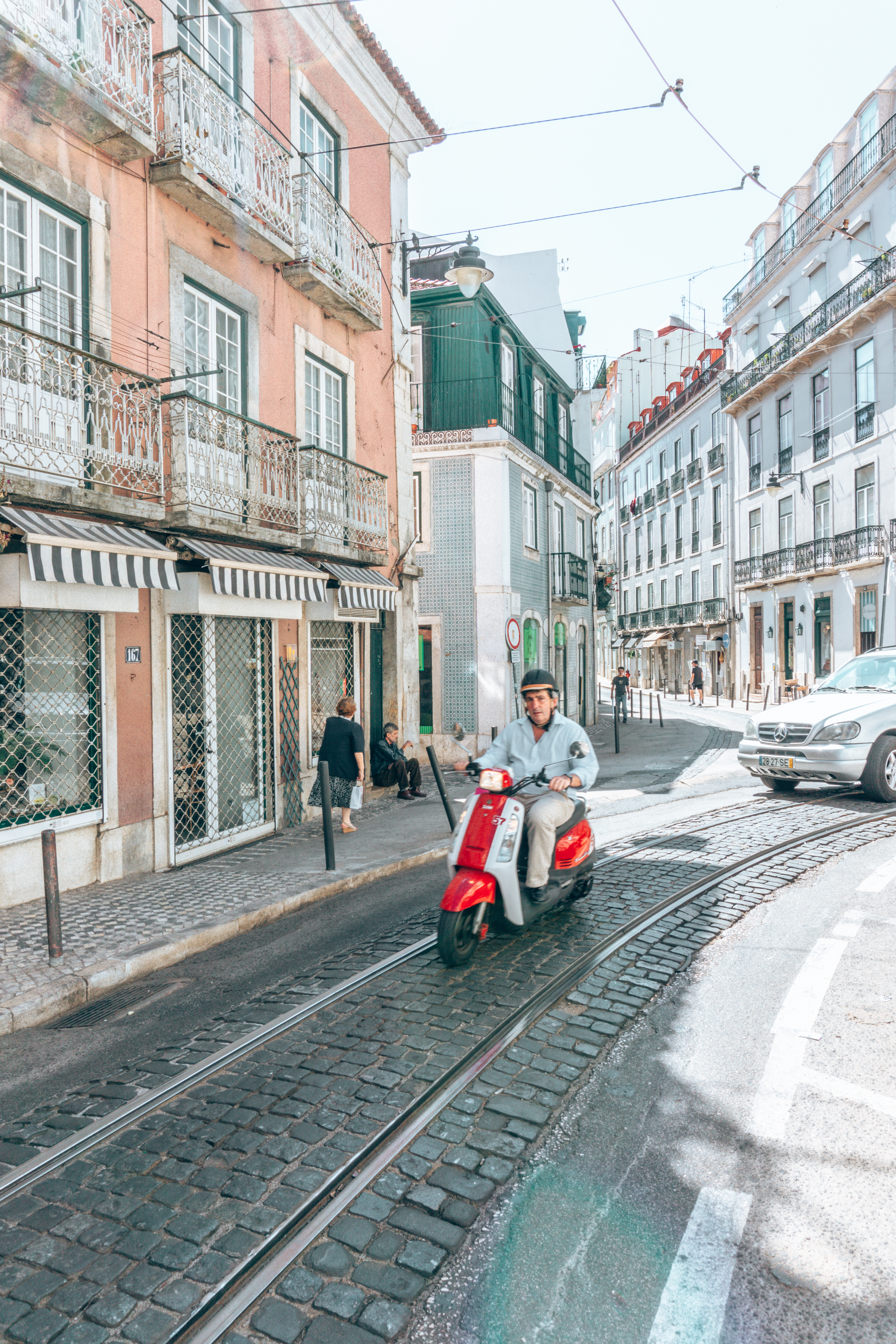 A man on a red vespa zooms through Lisbon's colourful streets
