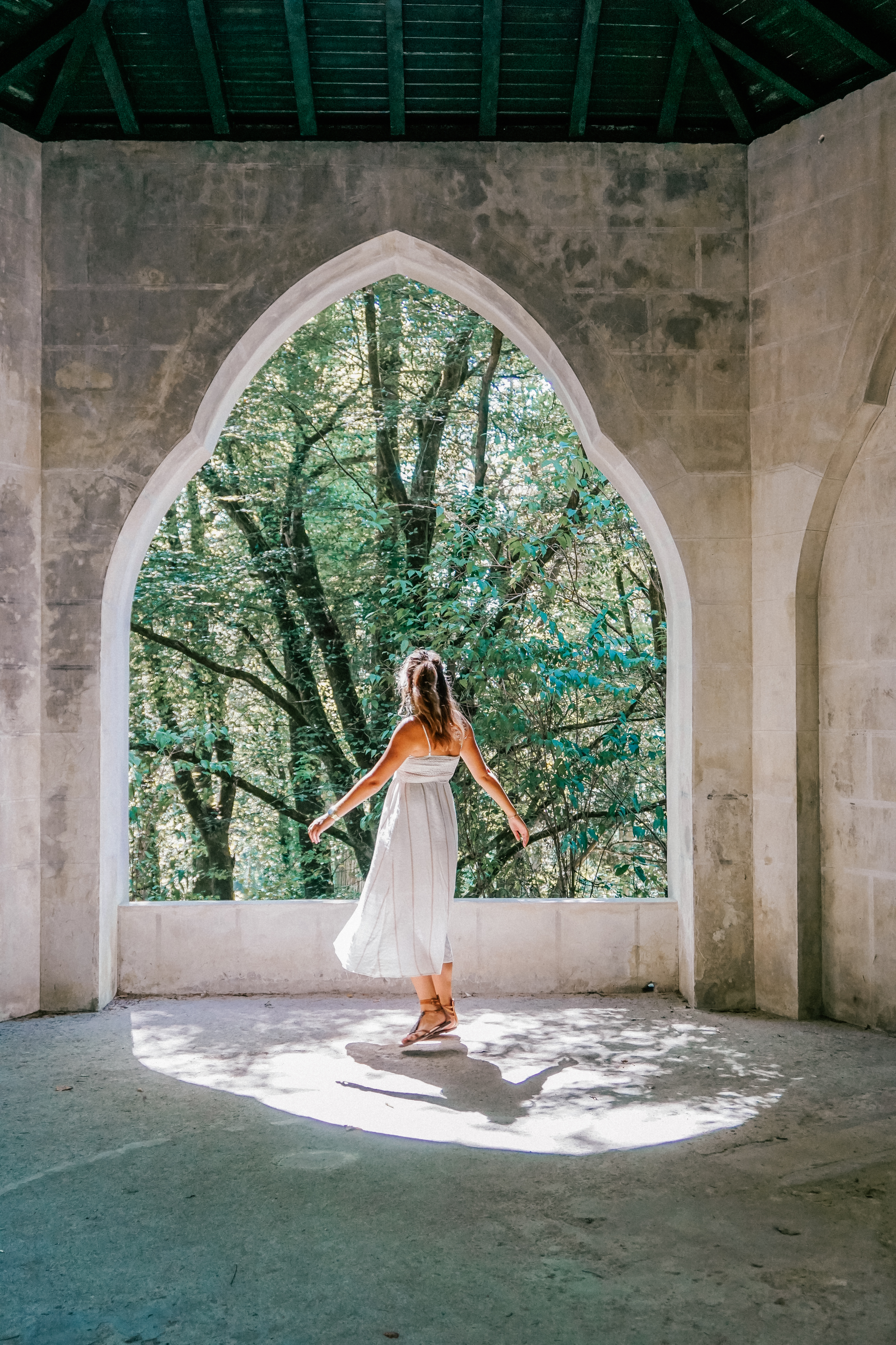 A girl in a white dress dances in the unique archway of sunlight in the Pena palace gardens. 