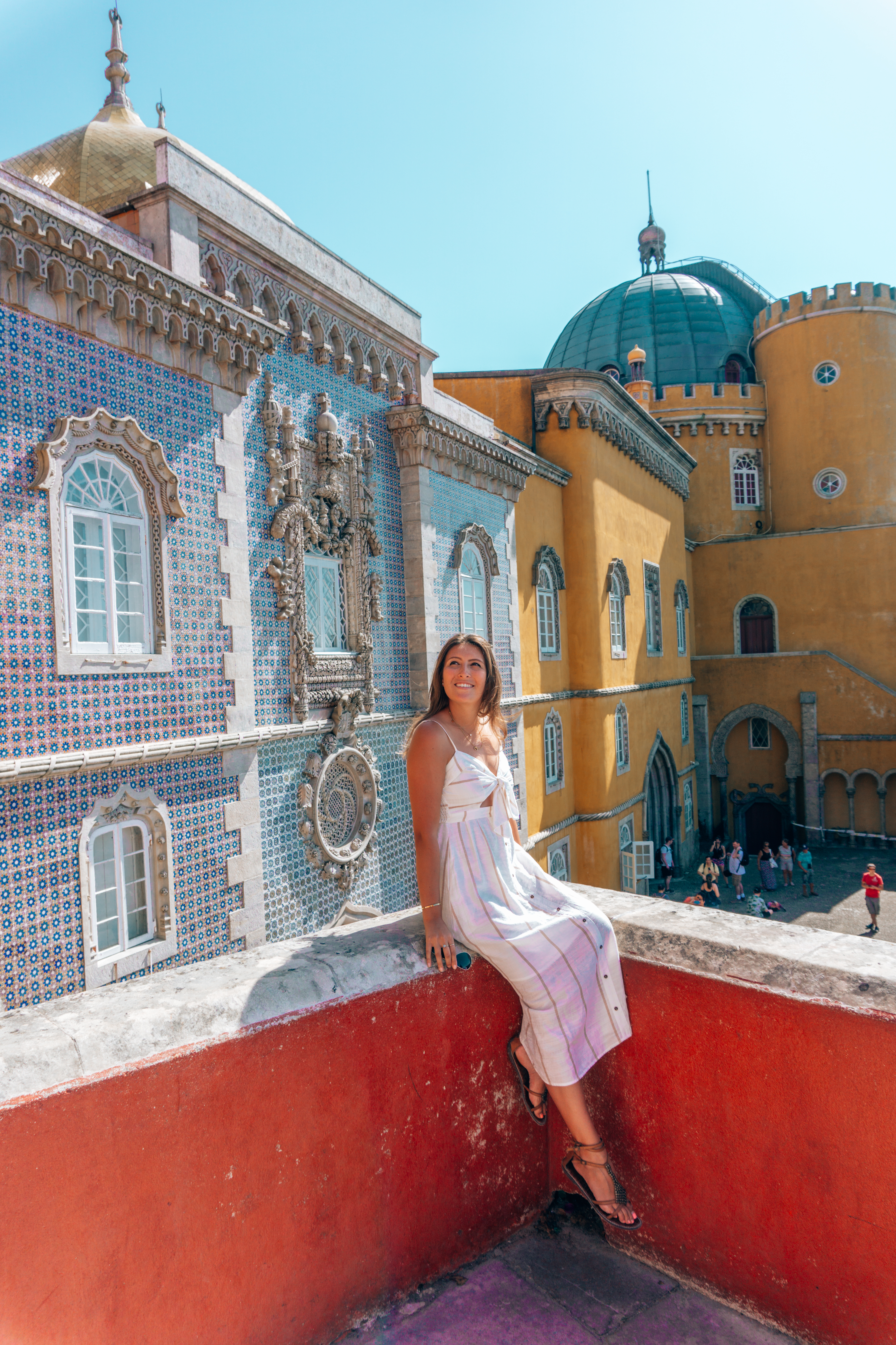 A girl in a white dress sits on a red ledge at the Pena Palace in Sintra, outside of Lisbon, Portugal.