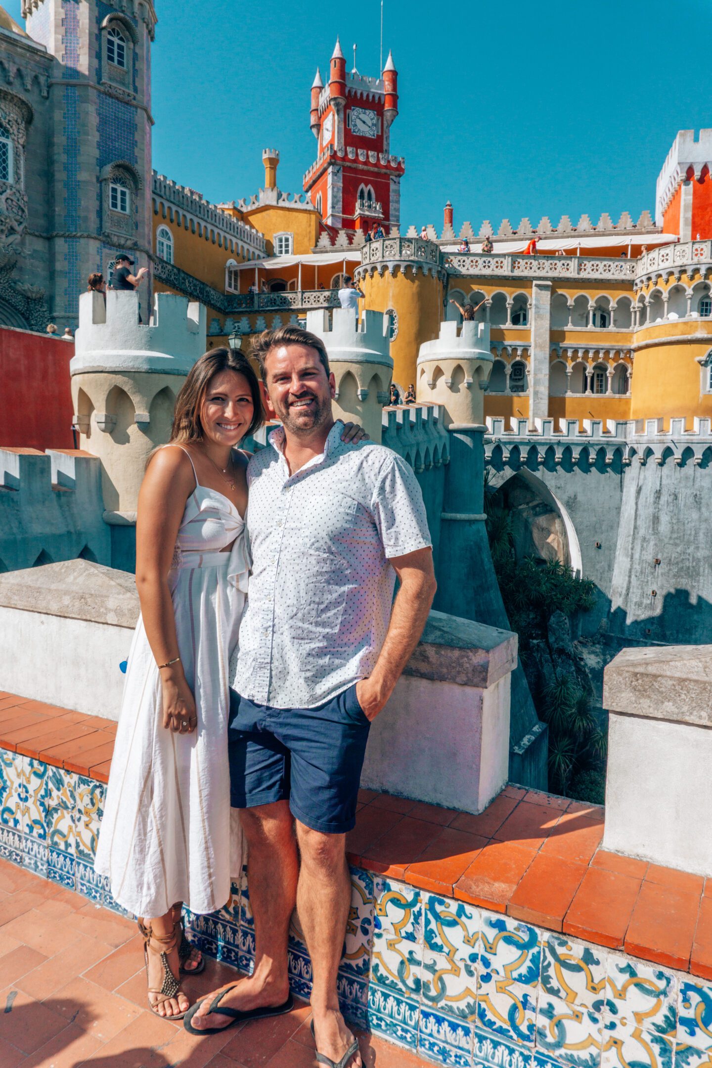 A couple smiles in front of Pena Palace in Sintra Portugal