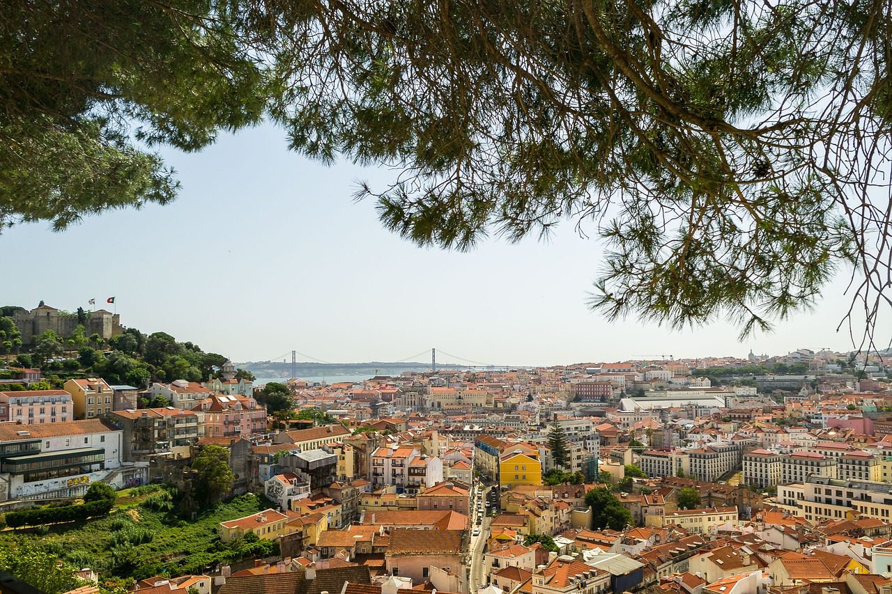 Looking over the colourful town of Lisbon, on a sunny summer day with the Ponte 25 de Abril bridge and São Jorge Castle to the left of the frame. 