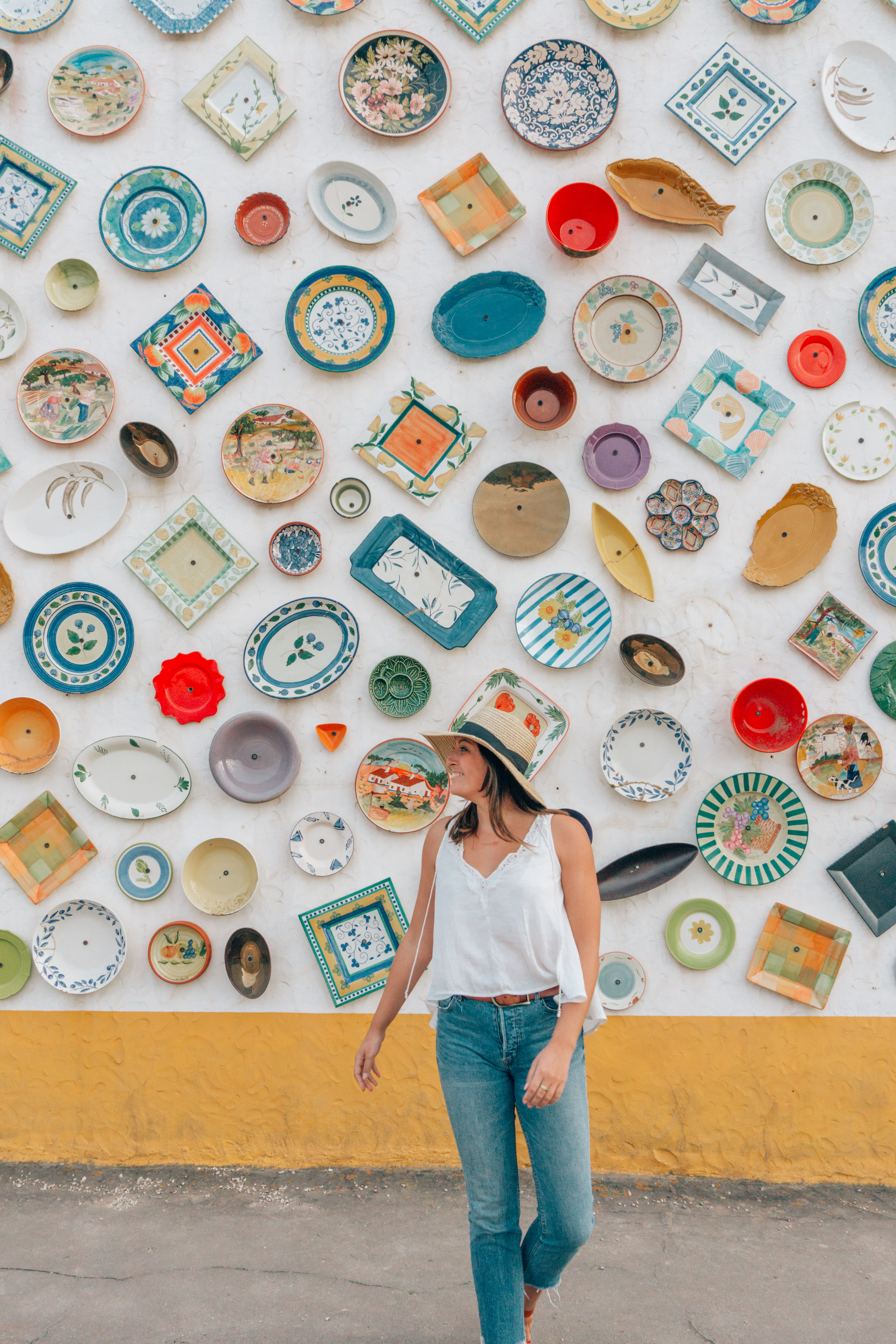 A girl in Lagos, Portugal smiling in front of a wall full of traditional Portuguese pottery because she used the Best Travel Planning Resources & Travel Gear I Swear By