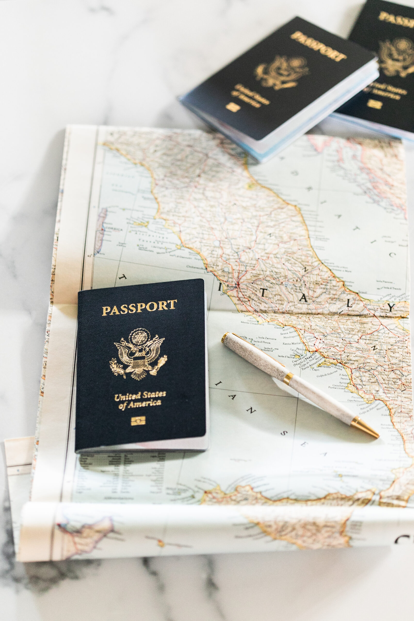A table with a map, pen and 3 USA passports. Should you use a travel agent or book your trip online?