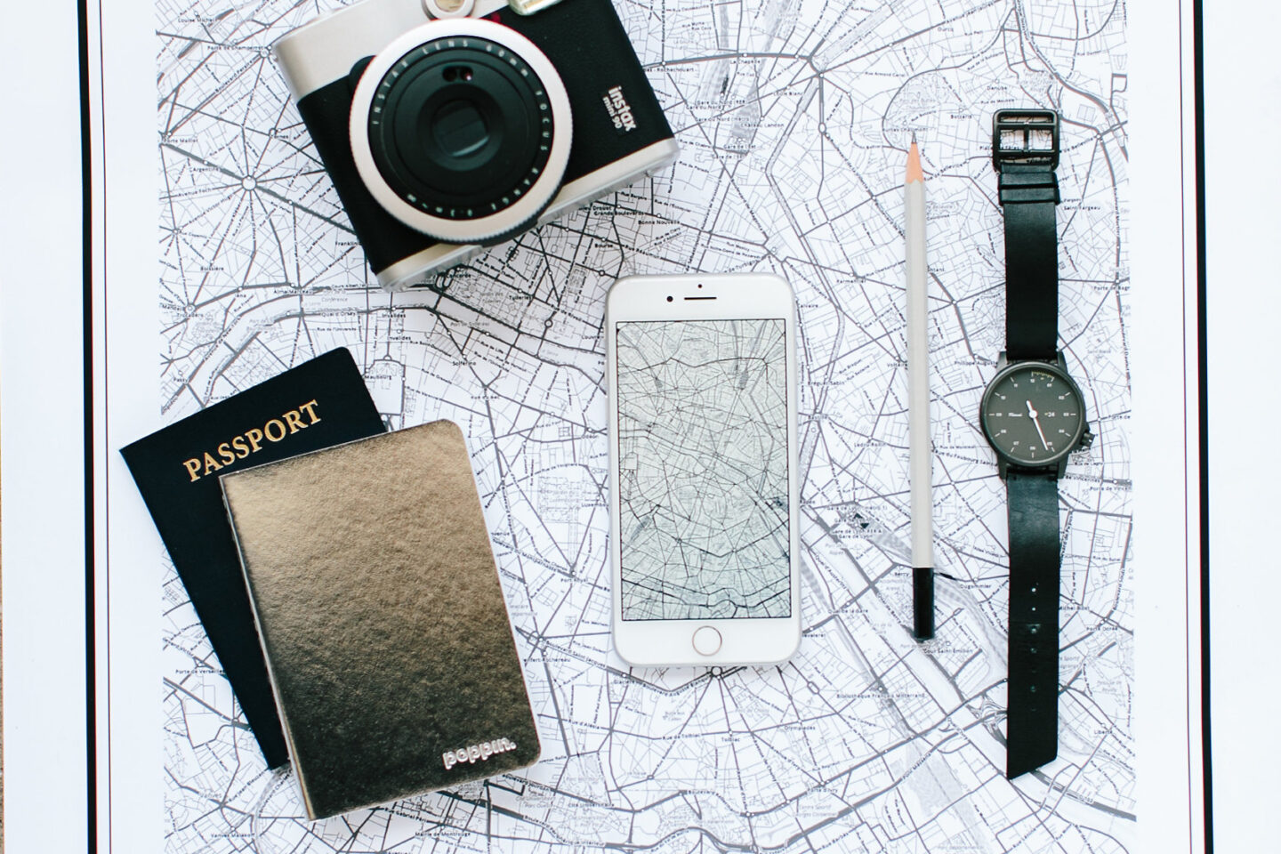 A black and white map of Paris is laid out on the table while Trip Planning with a passport, watch, iphone, and camera. How to Plan a Vacation on a Budget