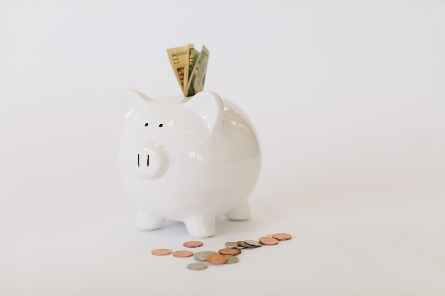 A white piggy bank with a money stuffed in the slot and coins on the side illustrate setting your vacation budget while trip planning. How to Plan a Vacation on a Budget