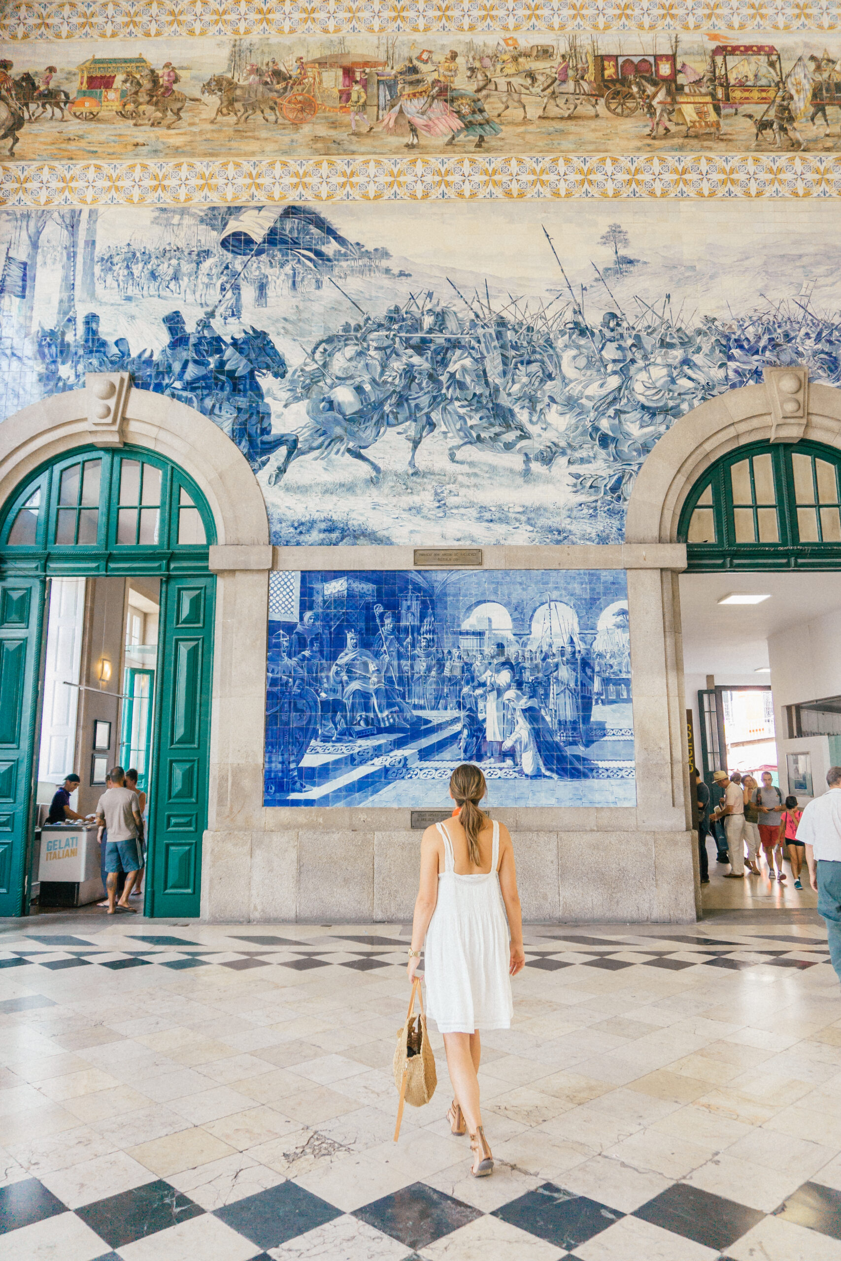 A girl in a white dress walks in São Bento Train Station, with beautiful tile work in Porto, Portugal