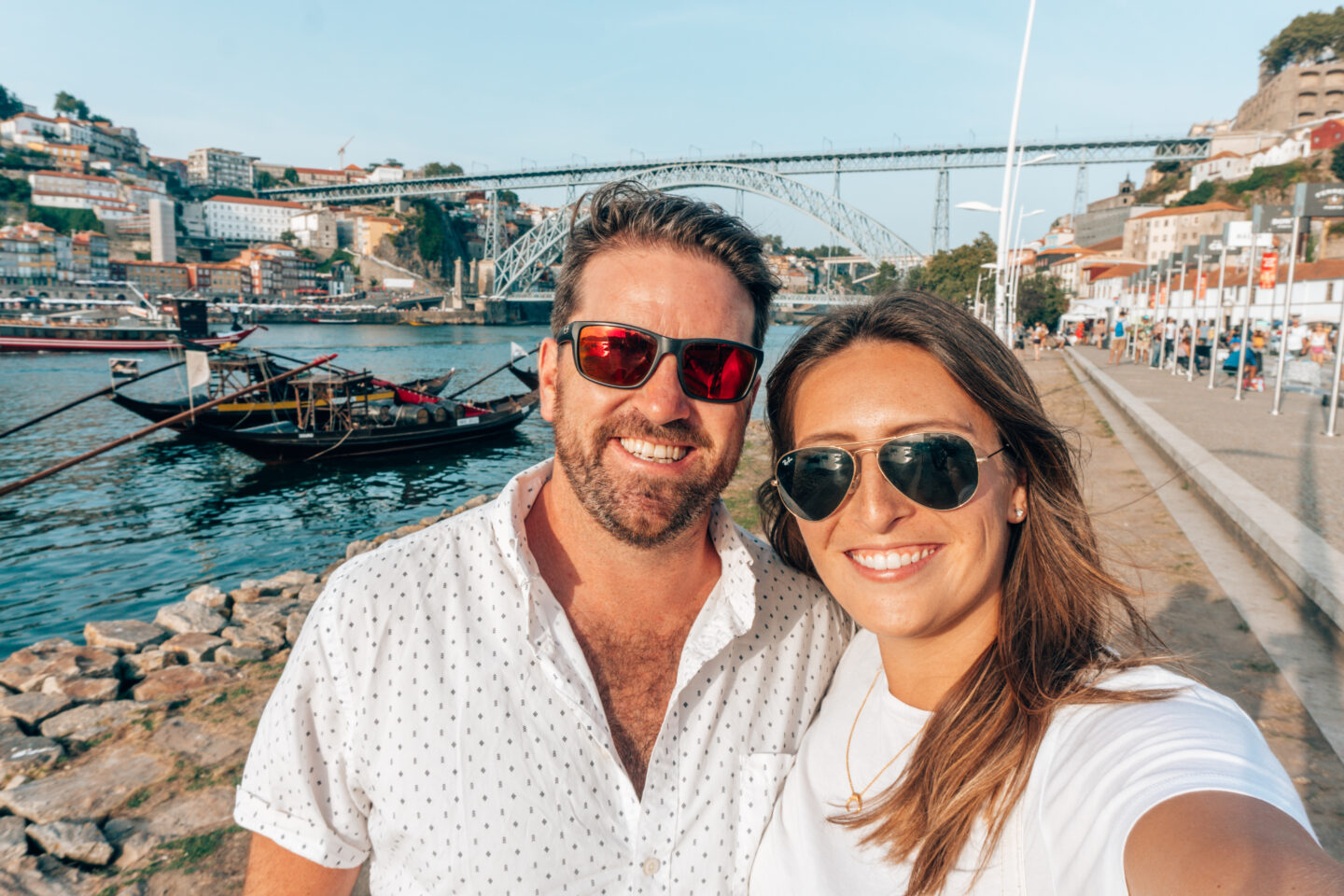 A couple wearing sunglasses take a selfie in front of the Dom Luís I Bridge in Porto, Portugal