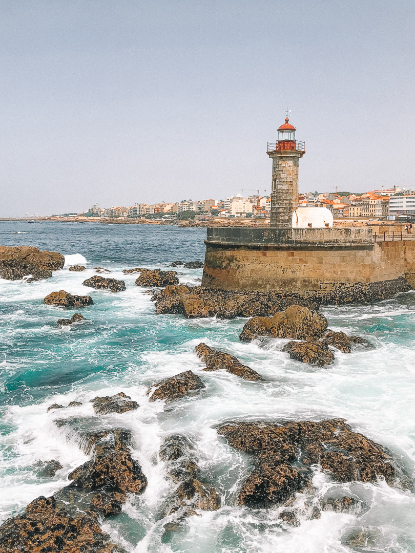 An old brick lighthouse with a red top, situated near the mouth of the Douro river, at the Foz do Douro neighbourhood coastline.