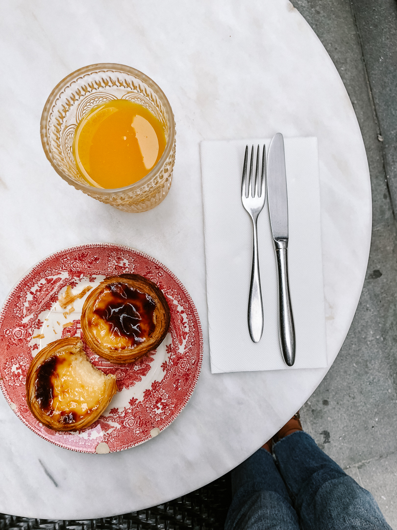 Two Portugese egg tarts (Pastel de Nata), and a cup of orange juice on a white marble cafe table in Porto
