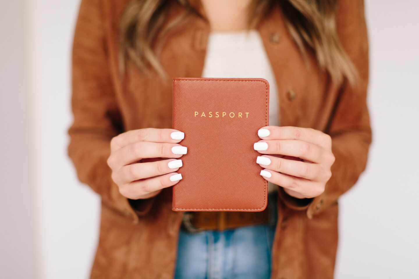 A girl with a brown jacket holds a passport in a brown leather passport holder. Stress Free Trip Planning Checklist: How to Plan a Vacation on a Budget