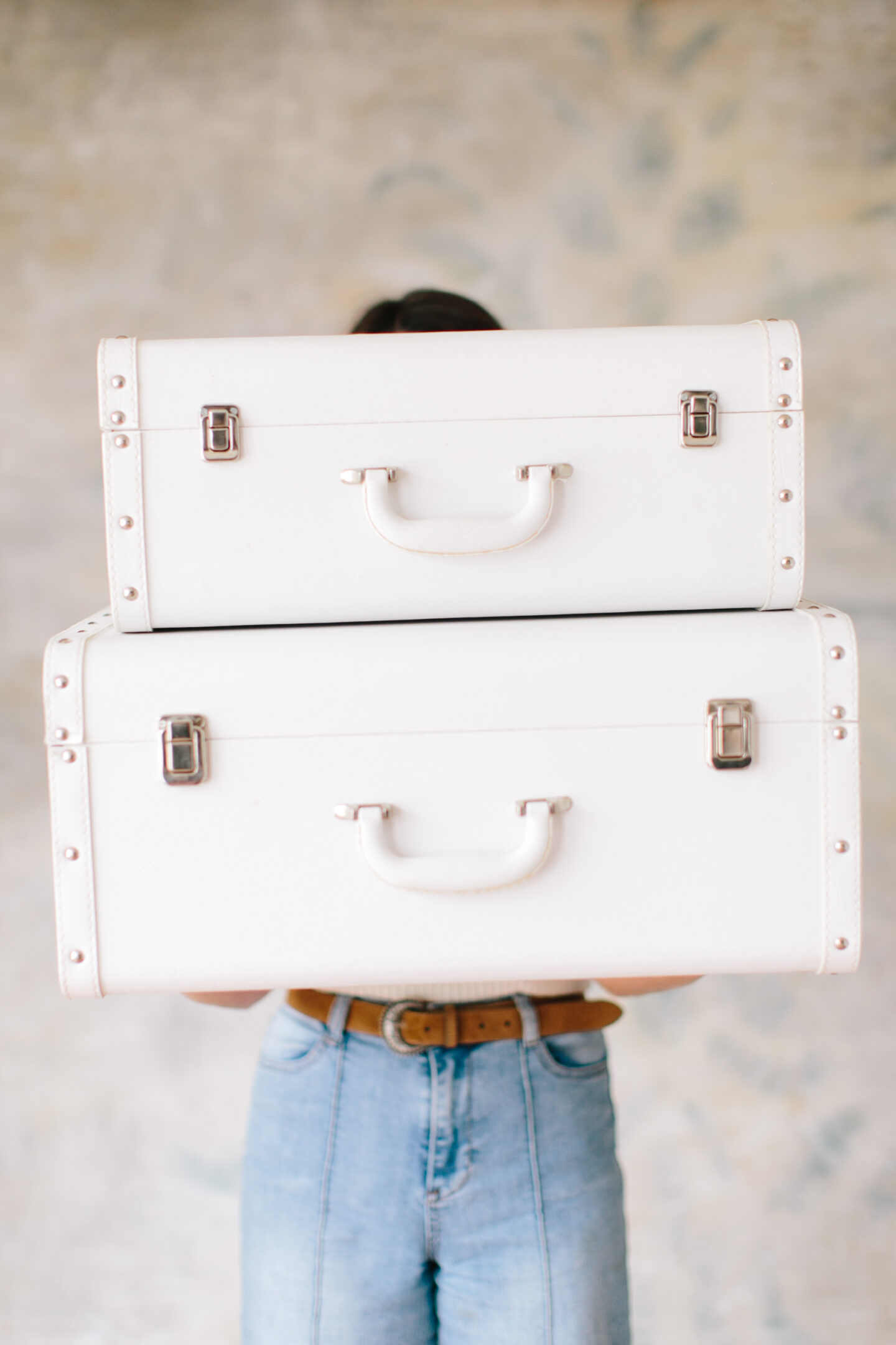 A girl holds two large vintage white suitcases while packing for her next trip!