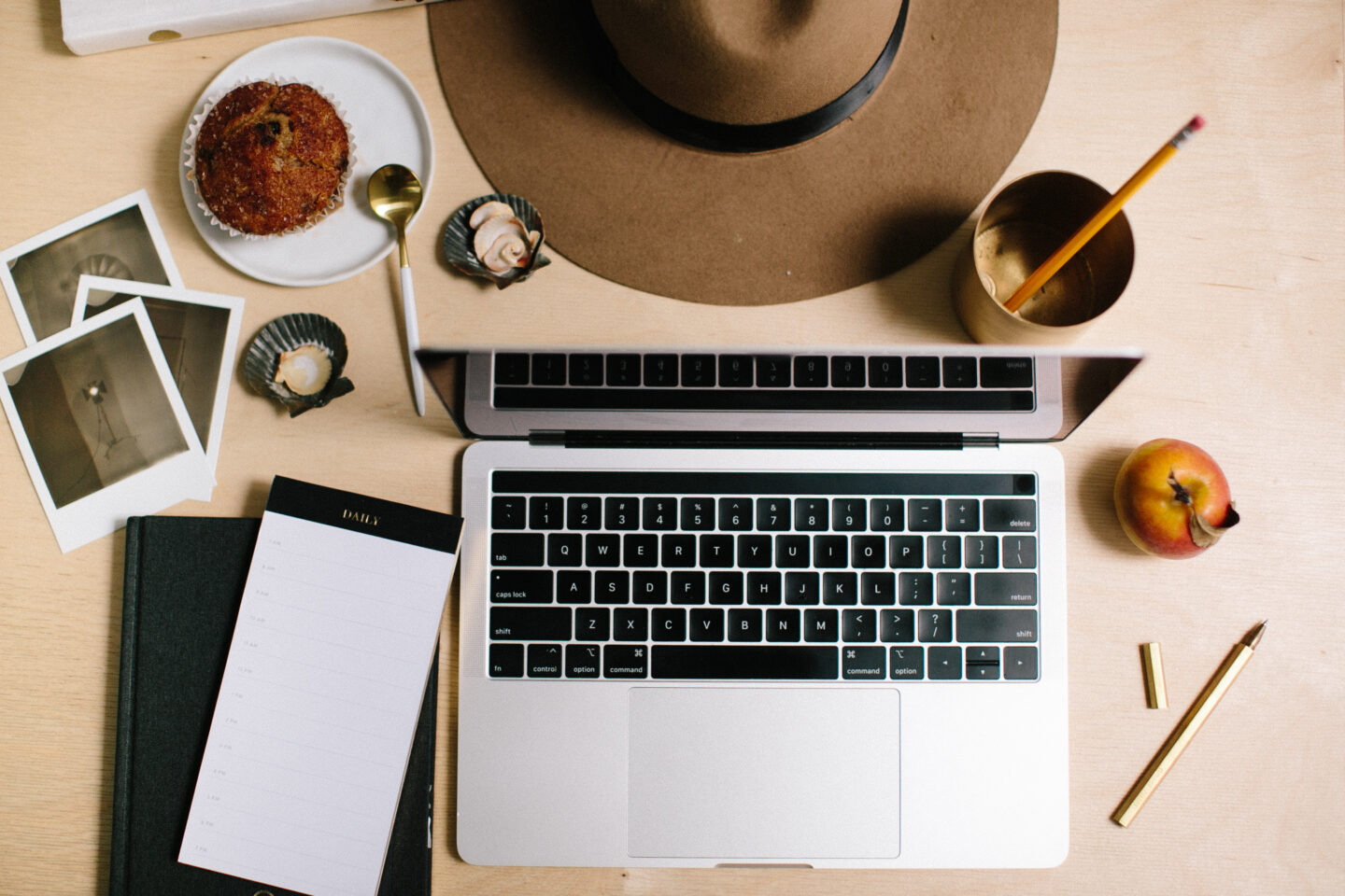 Looking down at a desk with a laptop, pen, notepad, apple, hat, and photos. Clearly someone is using this Trip Planning Checklist and planning a Vacation on a Budget