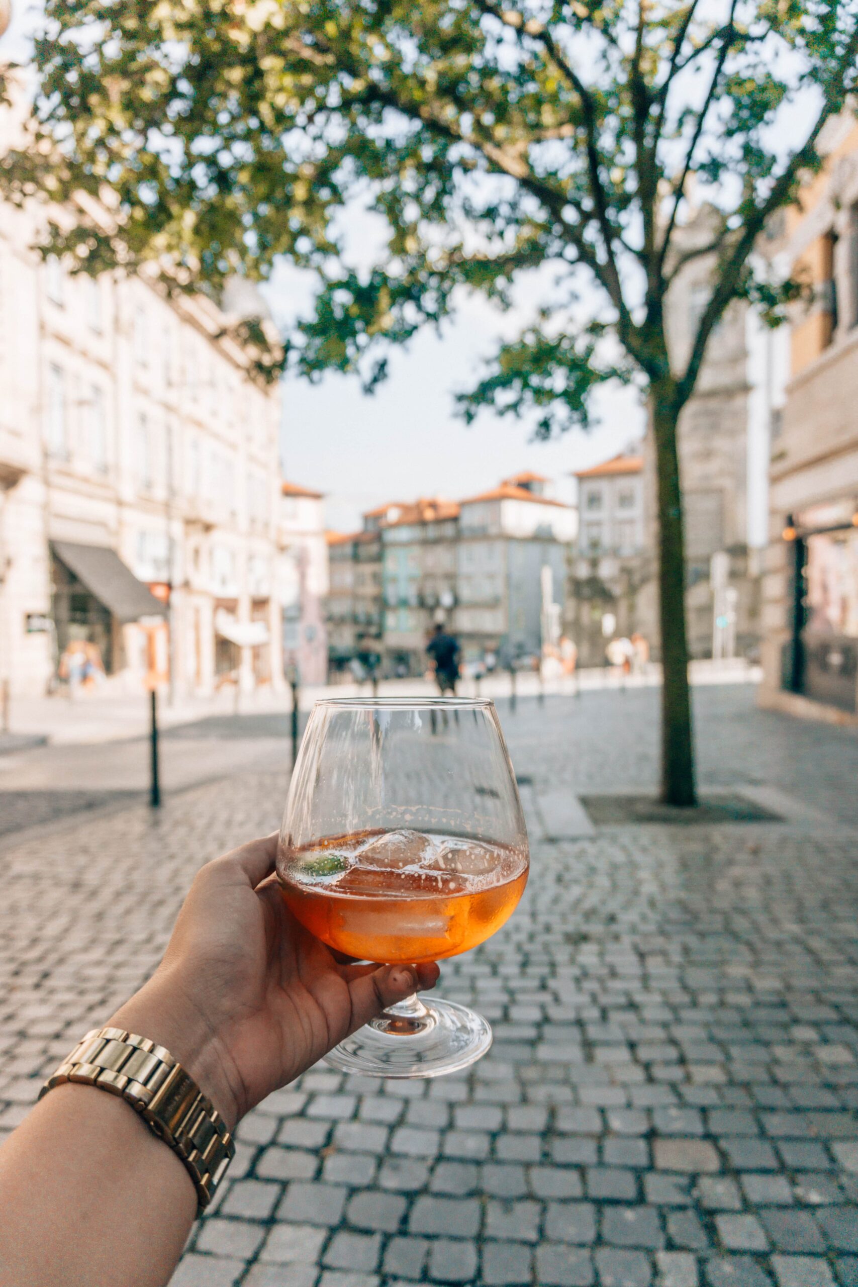 A girl with a golden watch holds a white port tonic cocktail in the heart of Porto, Portugal