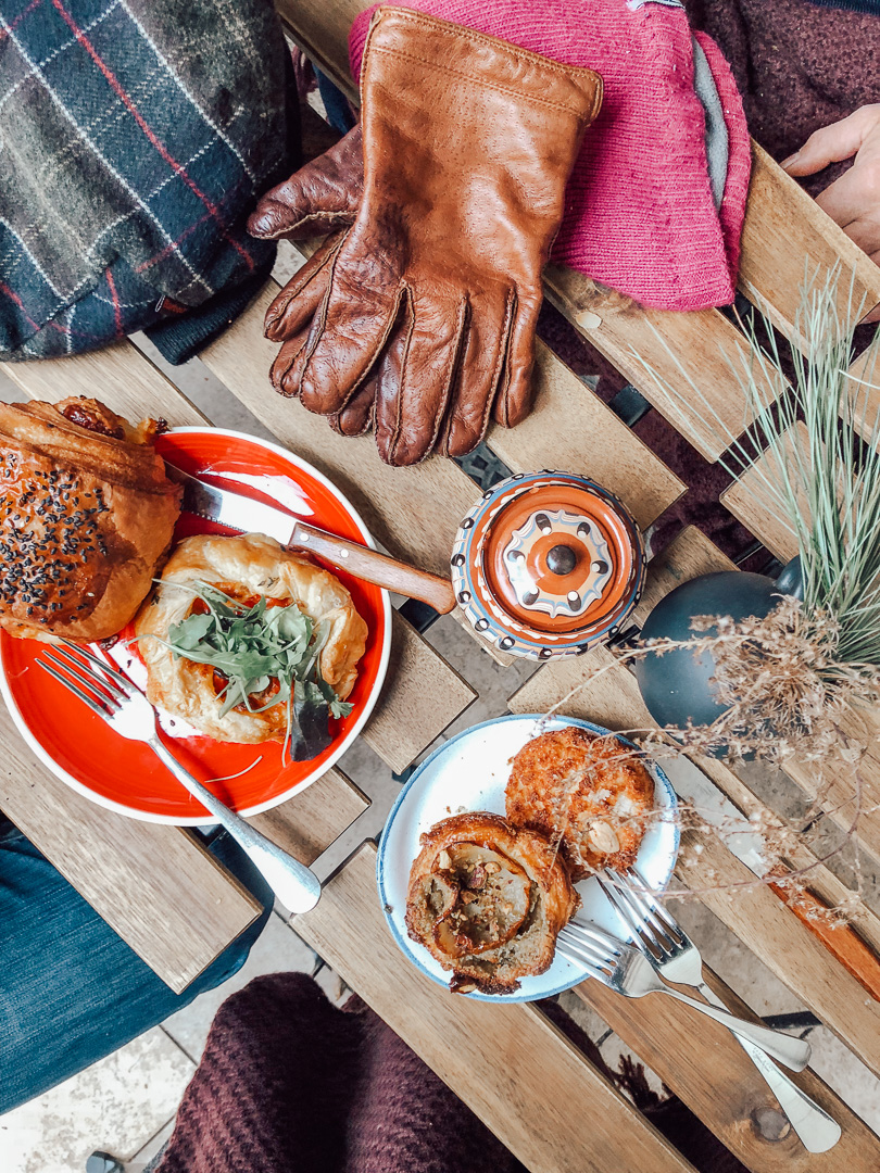 Looking down at our outdoor patio table with our delicious breakfast spread from Szalamibolt Cafe for Breakfast. Winter gloves and hats are on the table with pastries. 