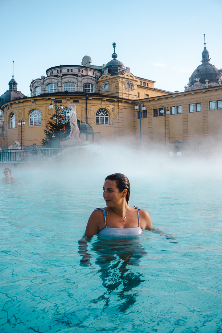 A girl smiles while immersed in the mineral rich waters of Széchenyi Thermal Bath house - a must-see during your 3 Days in Budapest Itinerary