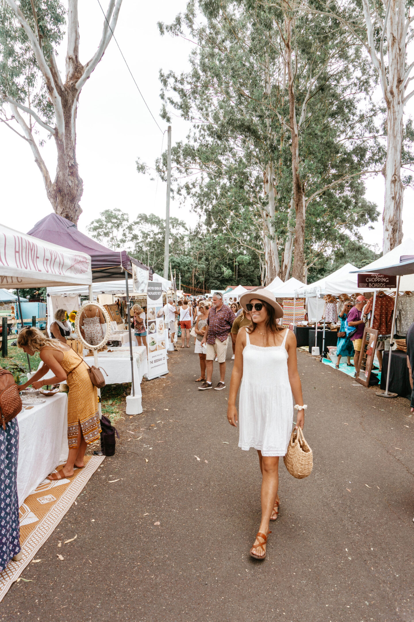 A girl wearing a white dress and hat walks through the famous Bangalow market; a must-do when visiting Byron Bay, Australia.
