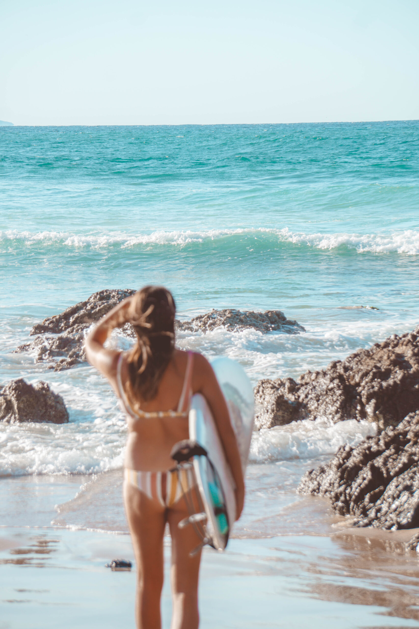 A surfer girls holds a surf board and looks out to the waves in Byron Bay