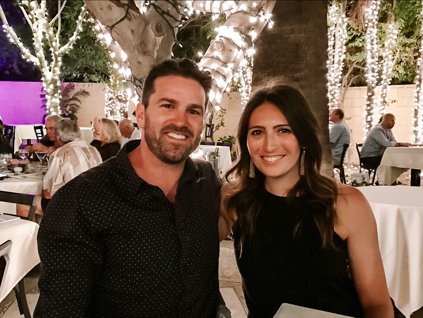 A couple sits in the lavender bistro surrounded by twinkle lights at night time. 